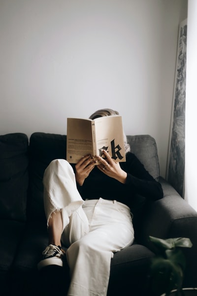 穿白衬衫的女人坐在黑沙发上看书